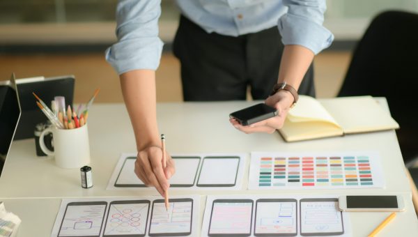 Cropped shot of young ux designer working on new application project while using smartphone in modern office room.